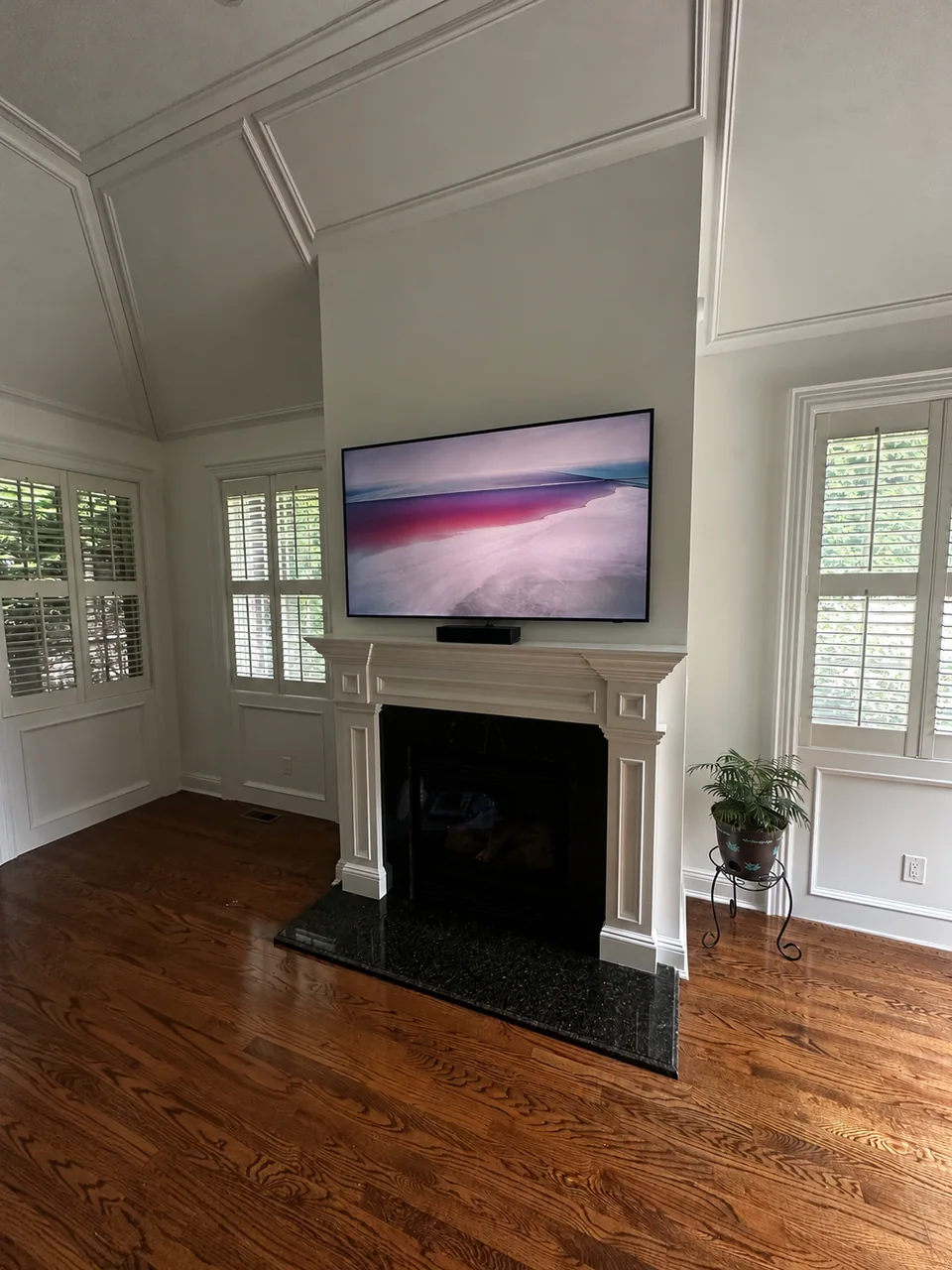 Wall-mounted TV above a white fireplace mantel; tools and packaging digitally removed