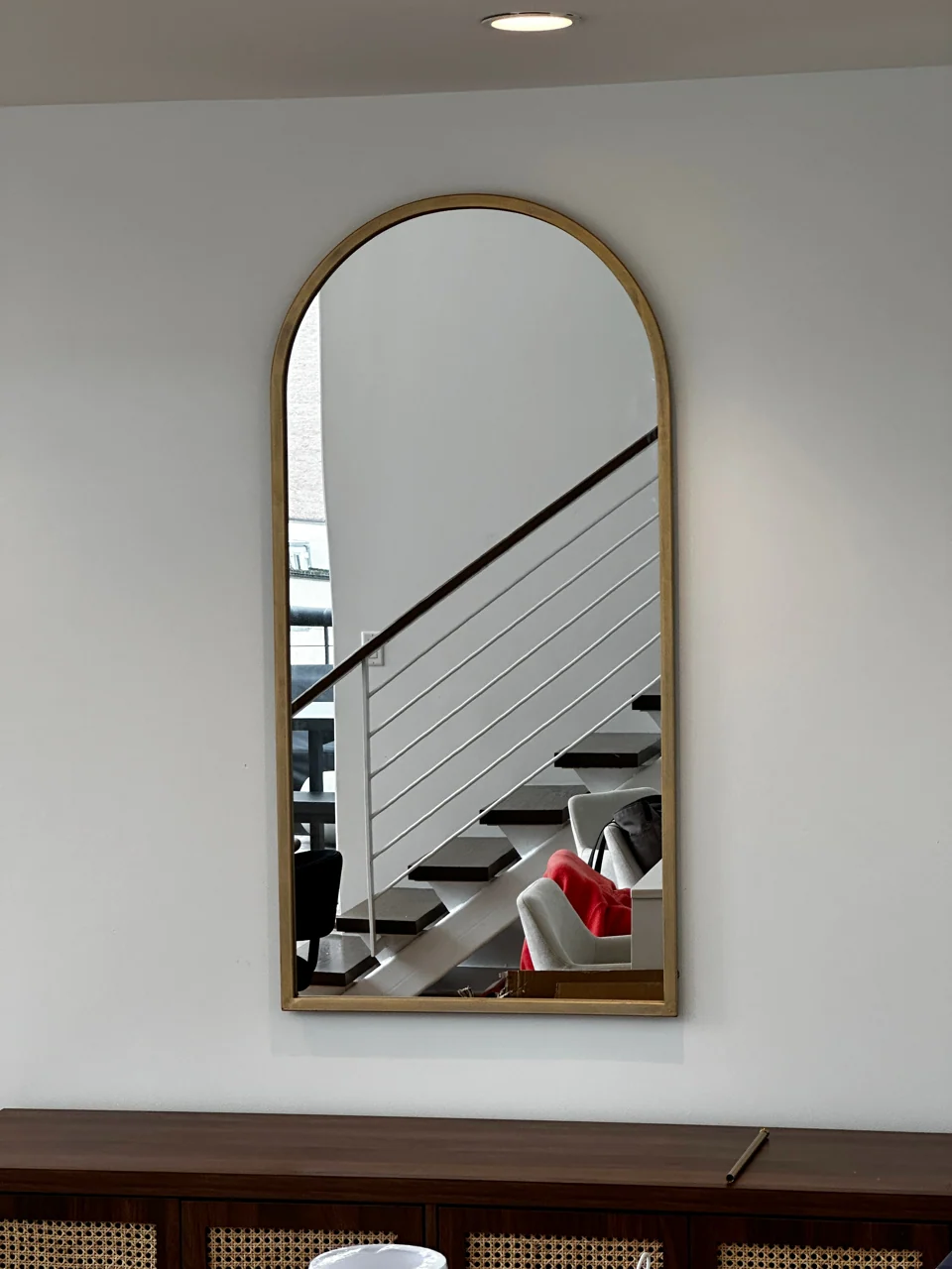 Tall gold-colored arched mirror reflecting a staircase