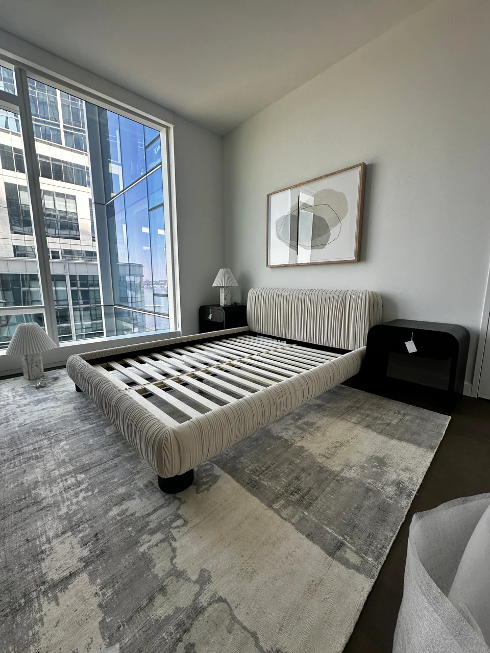 Upholstered bed frame with exposed slats beside large windows